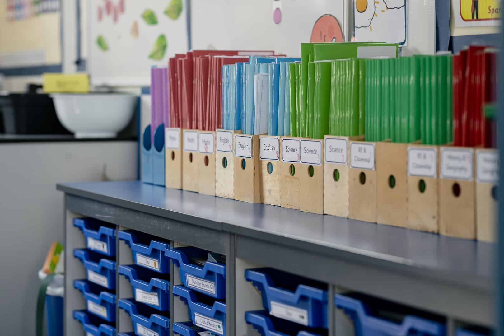 A close-up view of an organized classroom with color-organized wooden desk tidys lined up on the top of a set of classroom drawers. The school is based in Hexham in the North East of England.