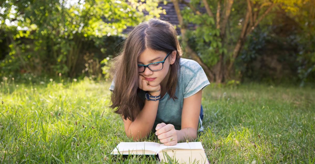 Girl lying on a meadow in garden reading book