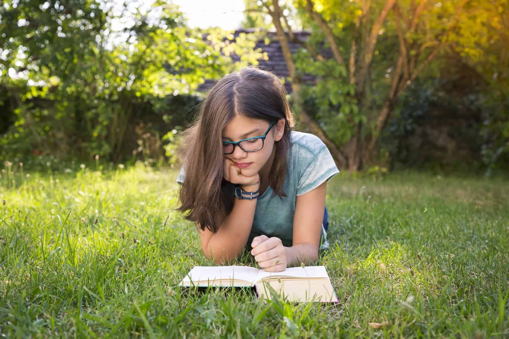 Girl lying on a meadow in garden reading book