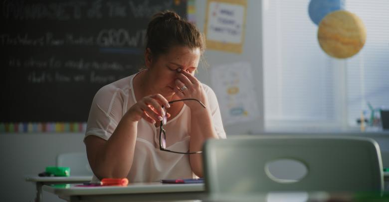 Tired Female Teacher Sitting Alone at the Desk in Empty Classroom, Relaxing After Class. Woman Feeling Stress, Burnout and Mental Exhaustion in Educational Environment, Working in Elementary School.