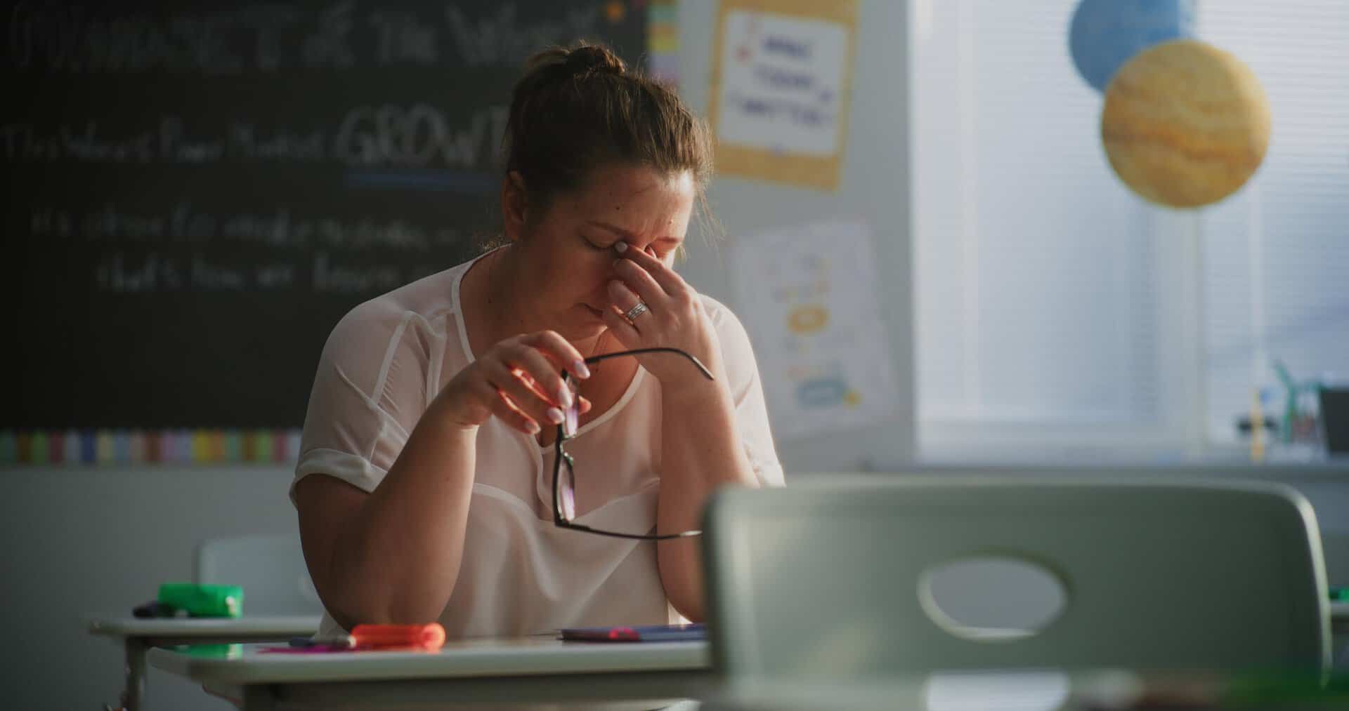 Tired Female Teacher Sitting Alone at the Desk in Empty Classroom, Relaxing After Class. Woman Feeling Stress, Burnout and Mental Exhaustion in Educational Environment, Working in Elementary School.