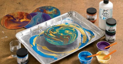 poured paint art project in foil pan, surrounded by acrylic paints and painting supplies