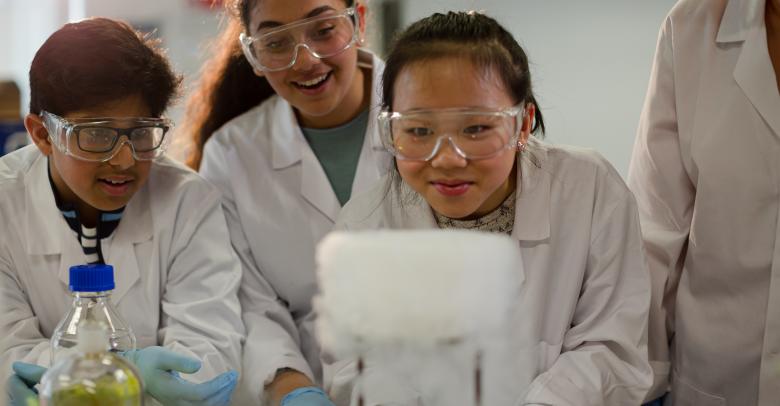 Female teacher and students watching scientific experiment chemical reaction in laboratory classroom