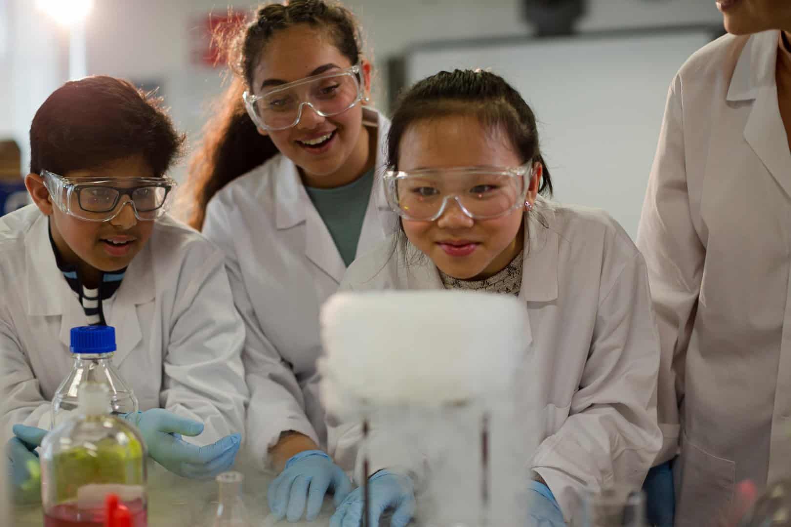 Female teacher and students watching scientific experiment chemical reaction in laboratory classroom