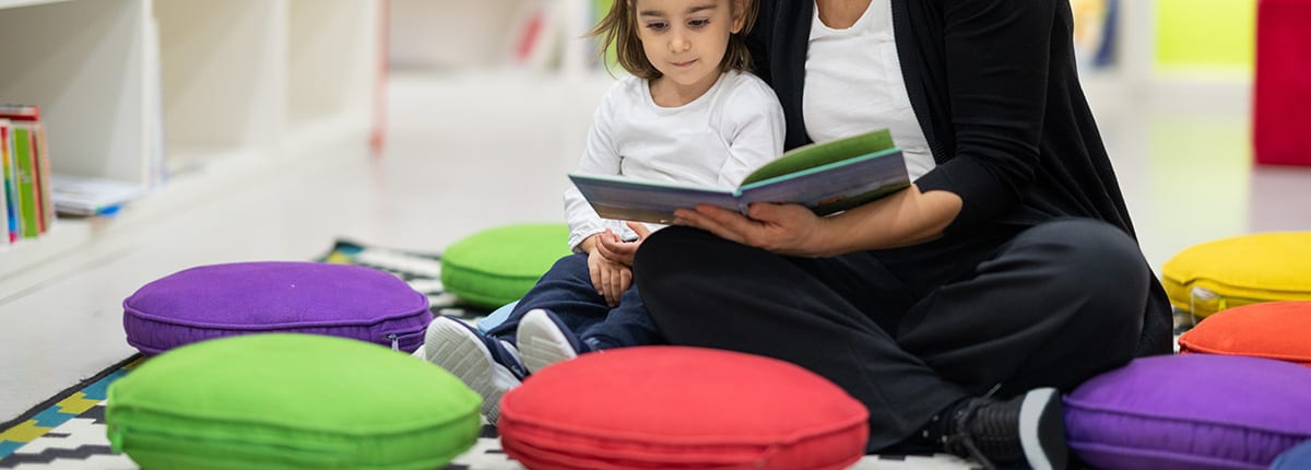 teacher and student reading surrounded by colorful floor cushions