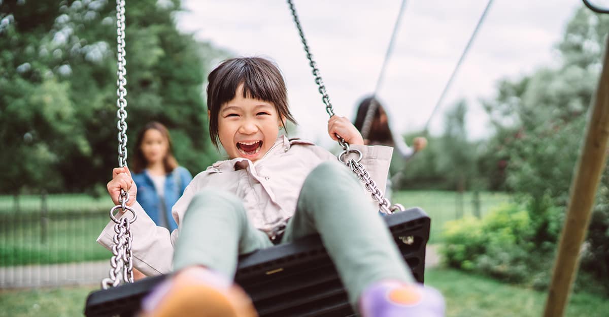 young girl smiling and laughing while playing on swing set