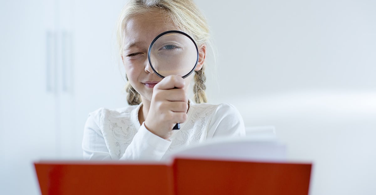 student close reading book with magnifying glass