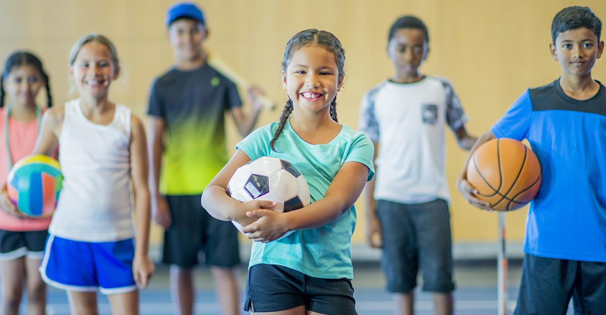 children in PE class holding different balls and sports equipment