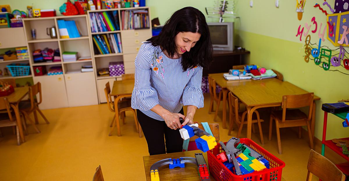 teacher picking up toys in early childhood preschool classroom