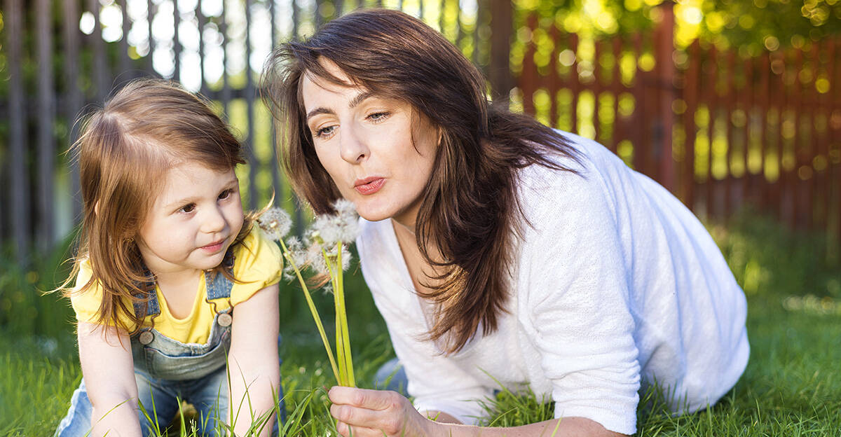 happy mother and daughter outside blowing on dandelions