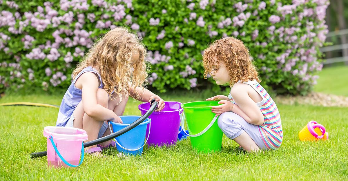 two girls in summer filling up buckets with water hose