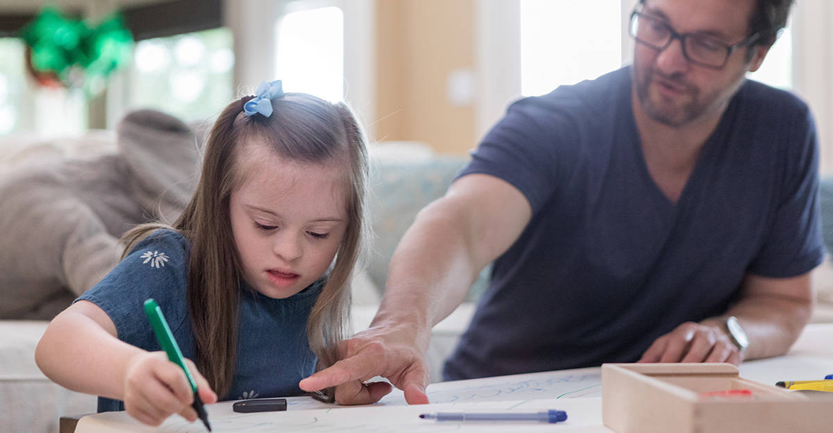 little girl with down syndrome practicing coloring with parent
