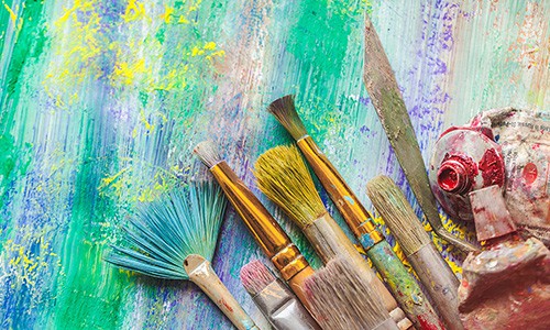 paint tubes, paintbrushes, and painting tools on colorful abstract background