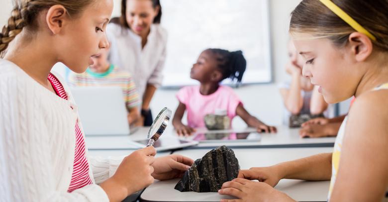 young earth science students in a classroom studying a rock