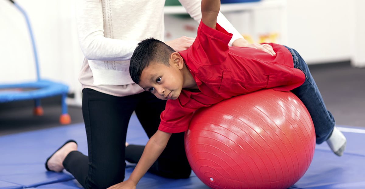 young boy using exercise therapy ball to practice motor skills