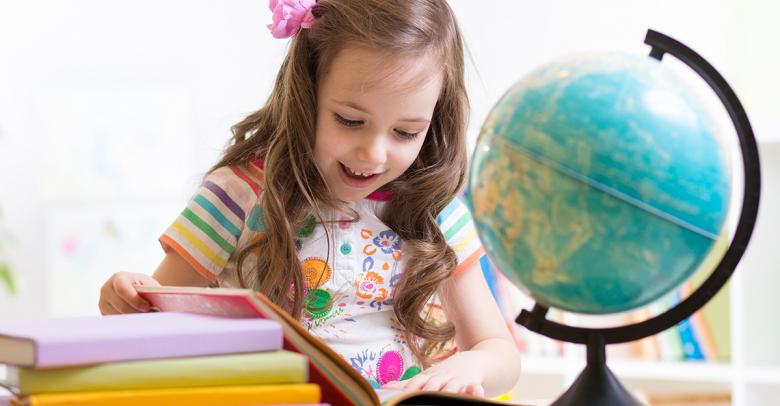 little girl reading earth day books next to globe