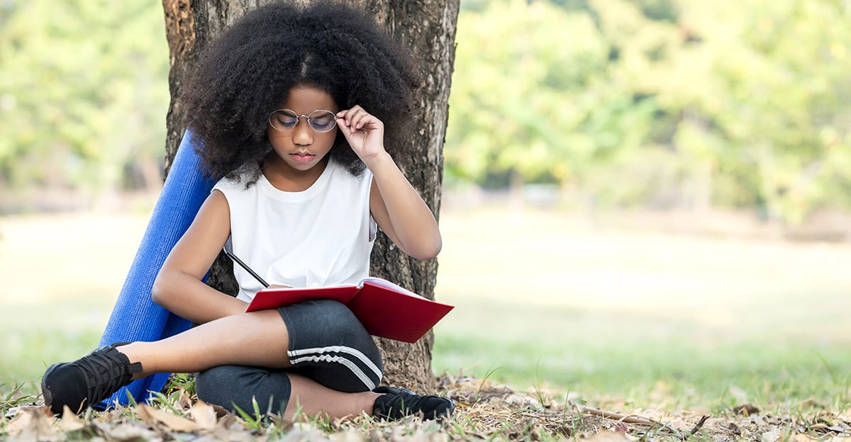 young girl reading and writing outside under tree