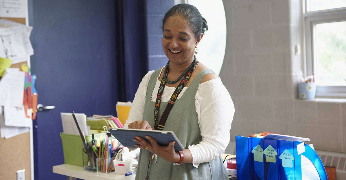 teacher smiling and reading digital tablet