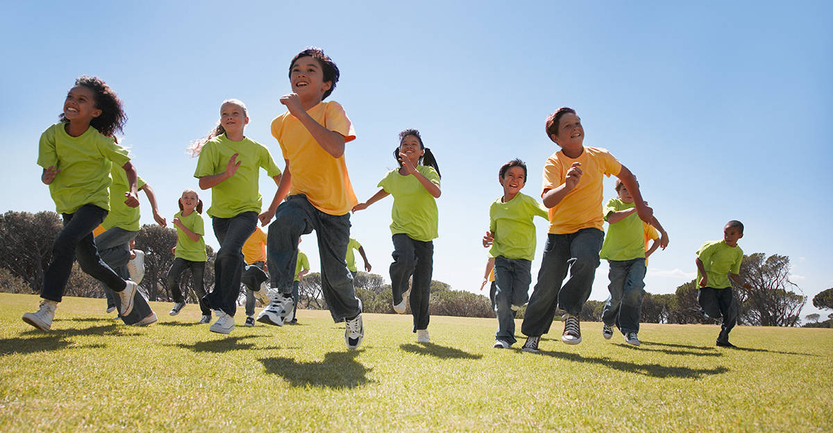 young smiling students participating in PE running activity outside on the grass