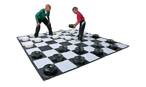 father and son playing checkers on a giant chess and checkers activity mat