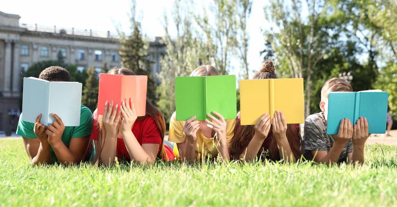 students learning outside in summer, laying on grass with books in front of their faces
