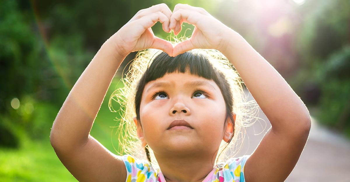little girl holding her hands up in the shape of a heart