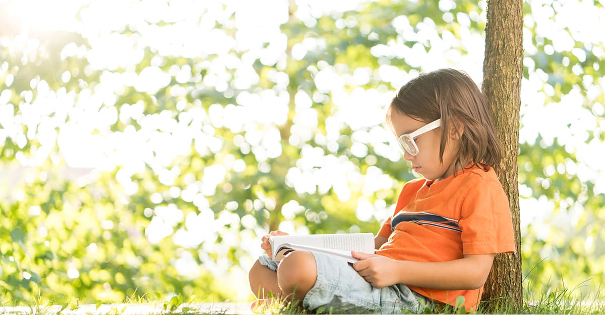 little boy reading a book and learning outdoors under a tree