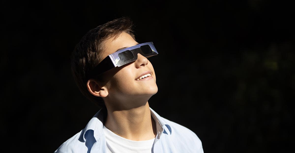 teenage boy looking up at solar eclipse with eclipse safety glasses