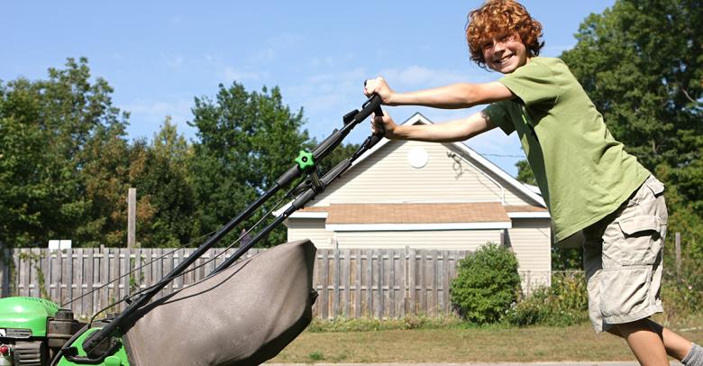 young kid smiling as he pushes a lawnmower