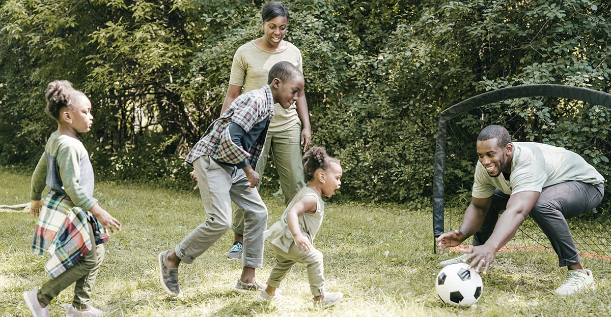 engaged family playing soccer together outside