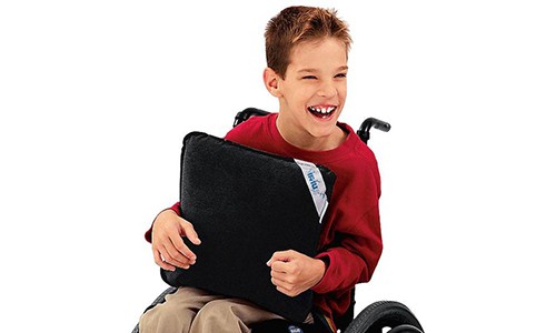 young smiling child in a wheelchair holding a vibrating pillow