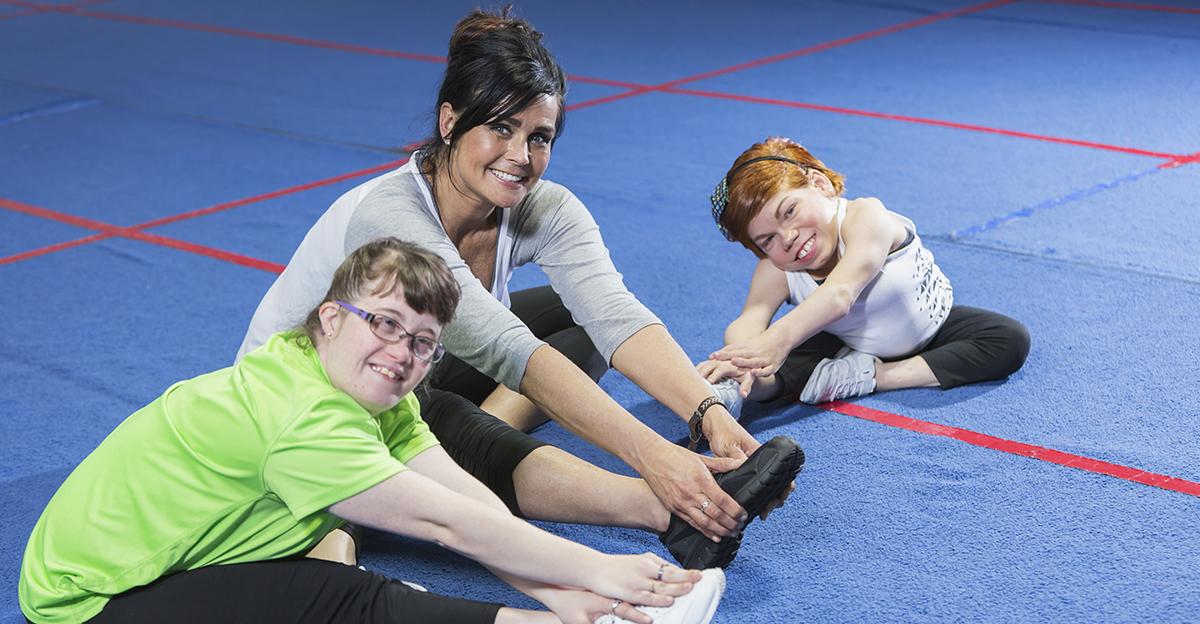 pe teacher and two girls with disabilities stretching together and smiling