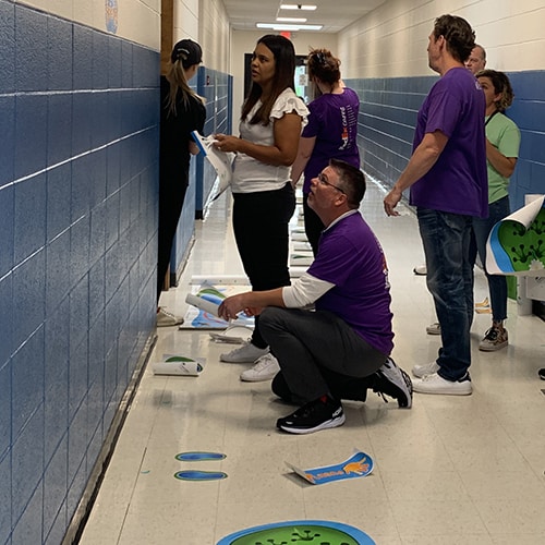 volunteers from the United Way, FedEx, and School Specialty installing sensory pathway stickers in an elementary school hallway