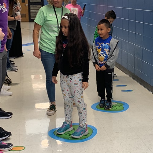elementary students standing on sensory pathways floor stickers in a school hallway