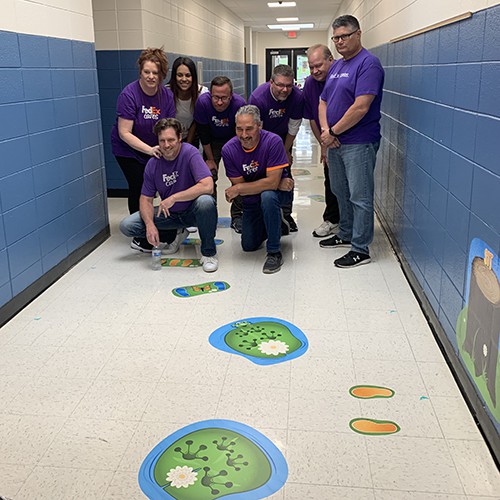 volunteers pose for picture after installing sensory pathways stickers in elementary school hallway