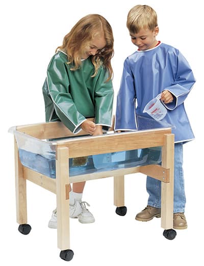 two children in art smocks playing in a sand and water table