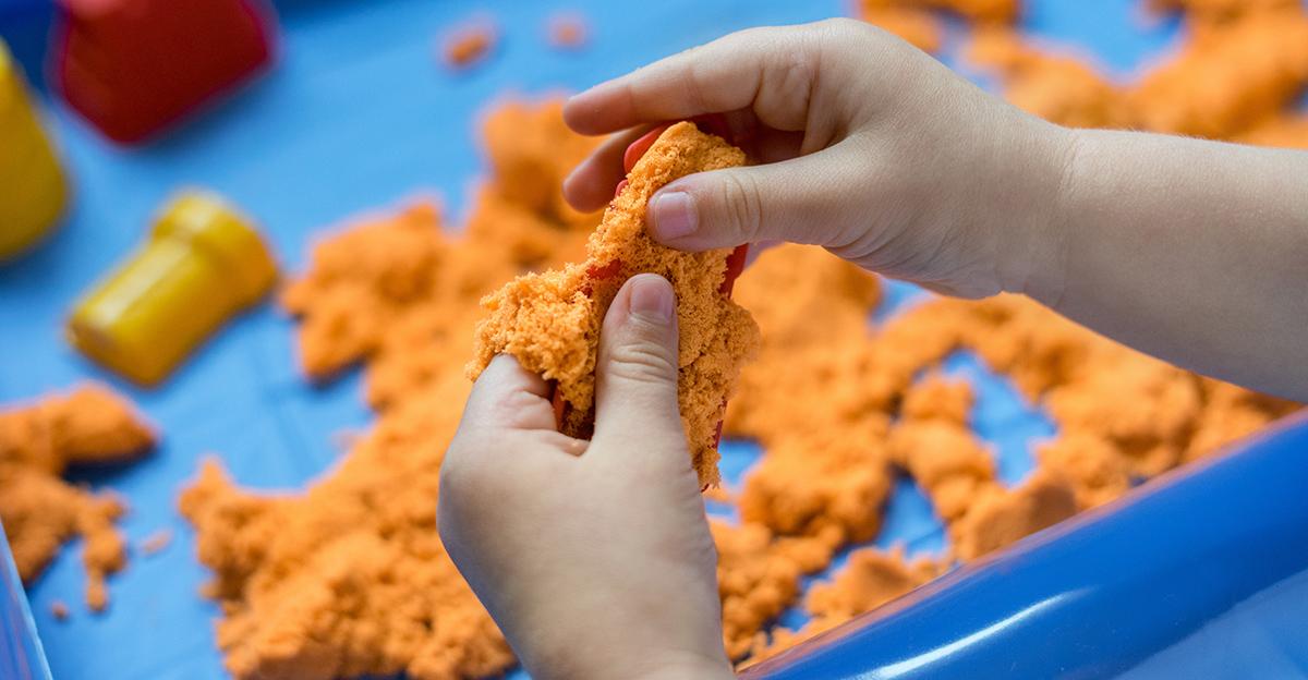 child's hands playing with orange sand as a sensory activity