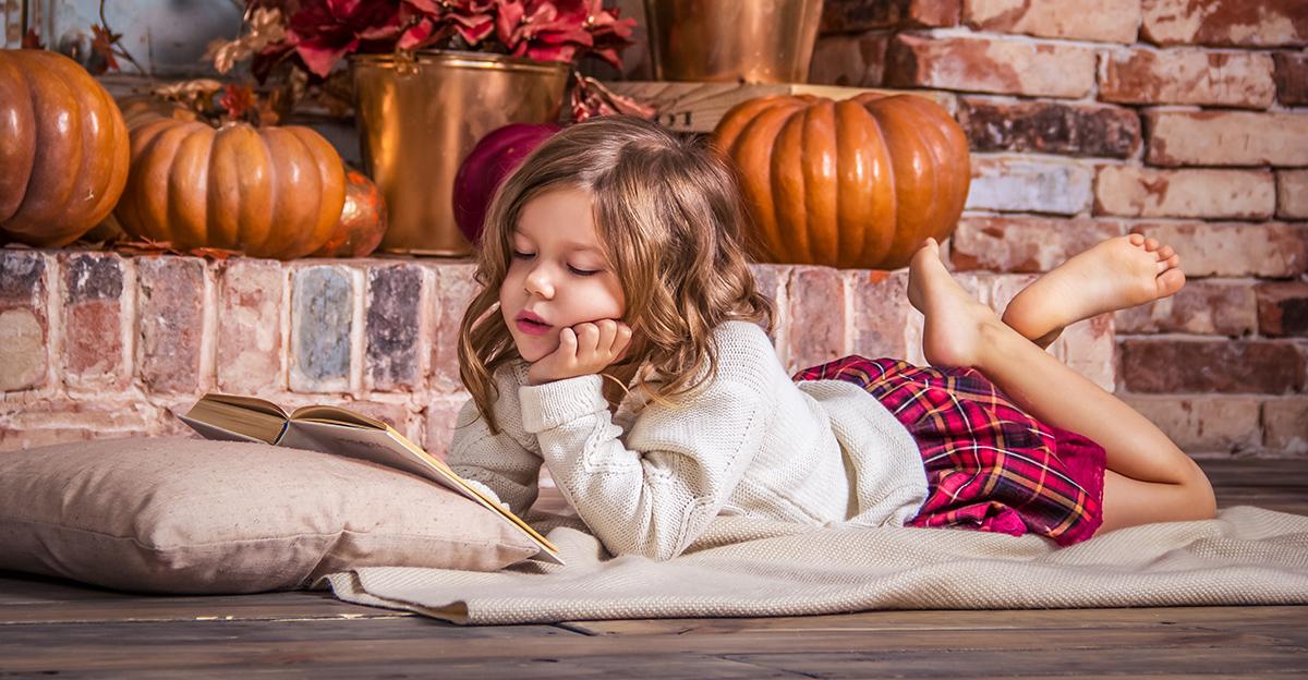 young girl reading a book with pumpkins in the background