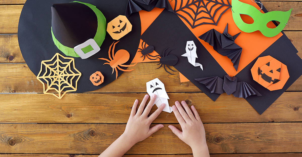 young student hands working on creating a halloween-themed origami ghost and bats