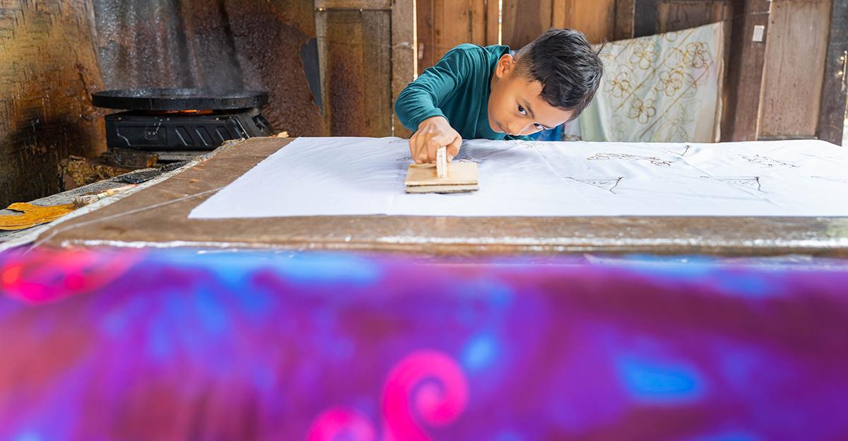 young student using a wax stamp to create batik art designs