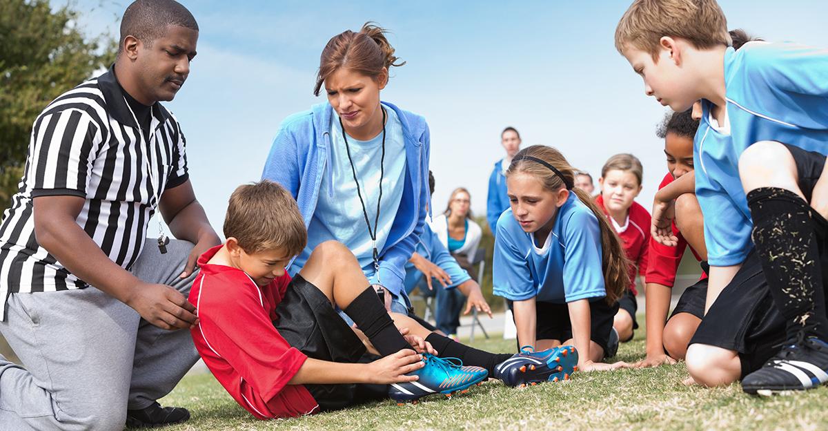 coach and referee tend to an injuries youth soccer player's sports injury, as other soccer players look on