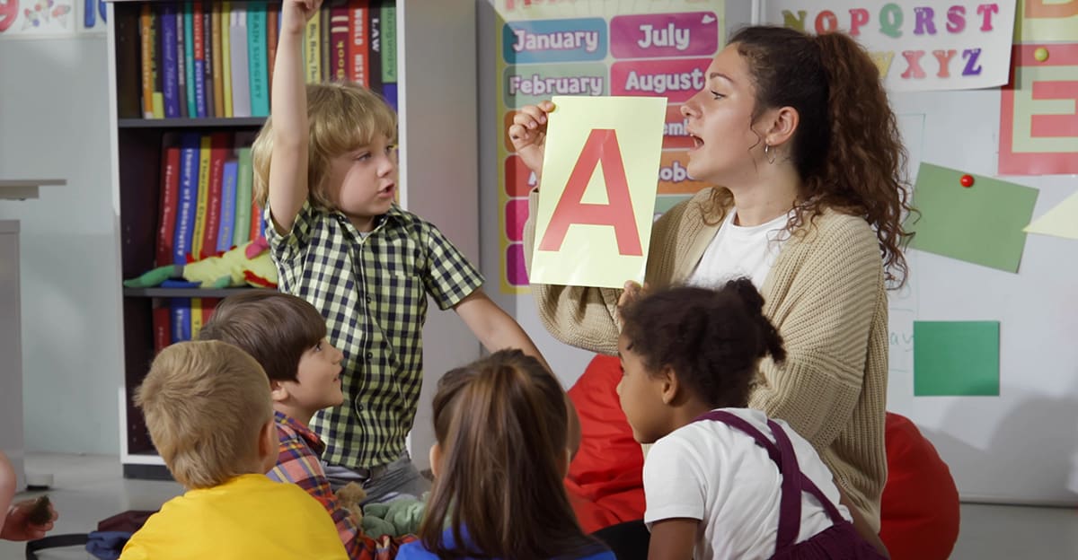 teacher holding up a flashcard with the letter a, teaching the alphabet to early childhood students
