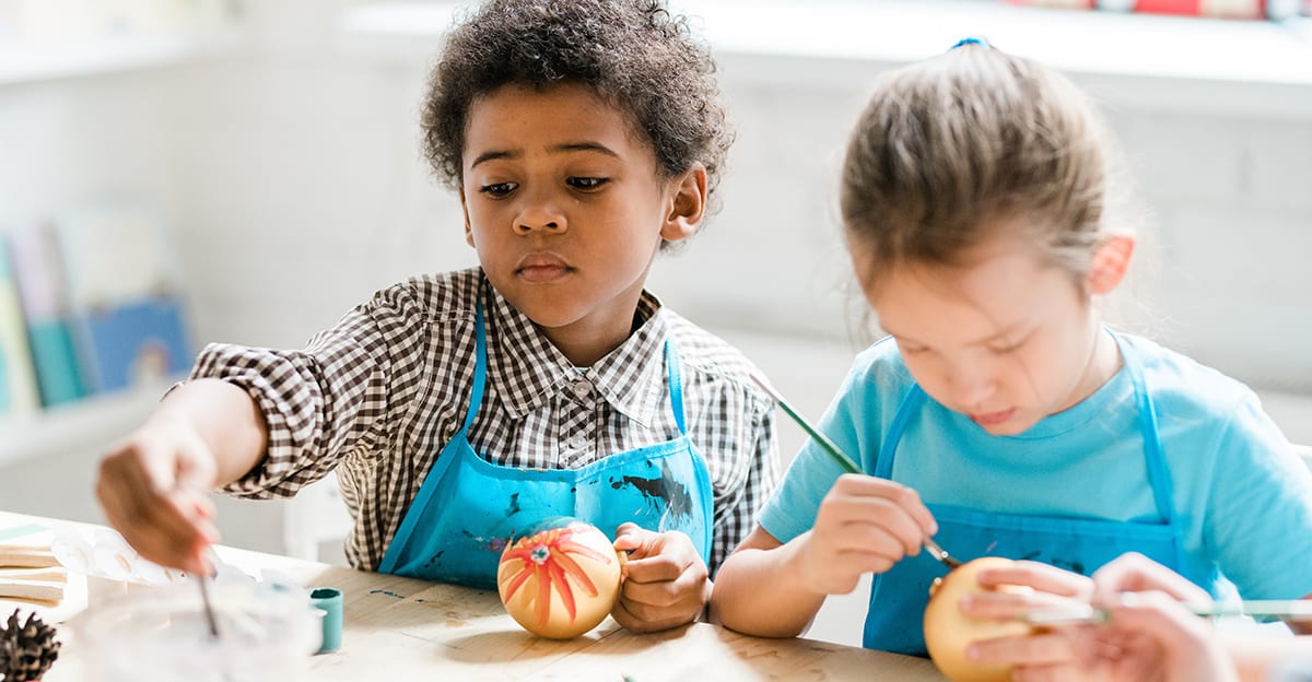 two young students in aprons painting ball ornaments for the holidays