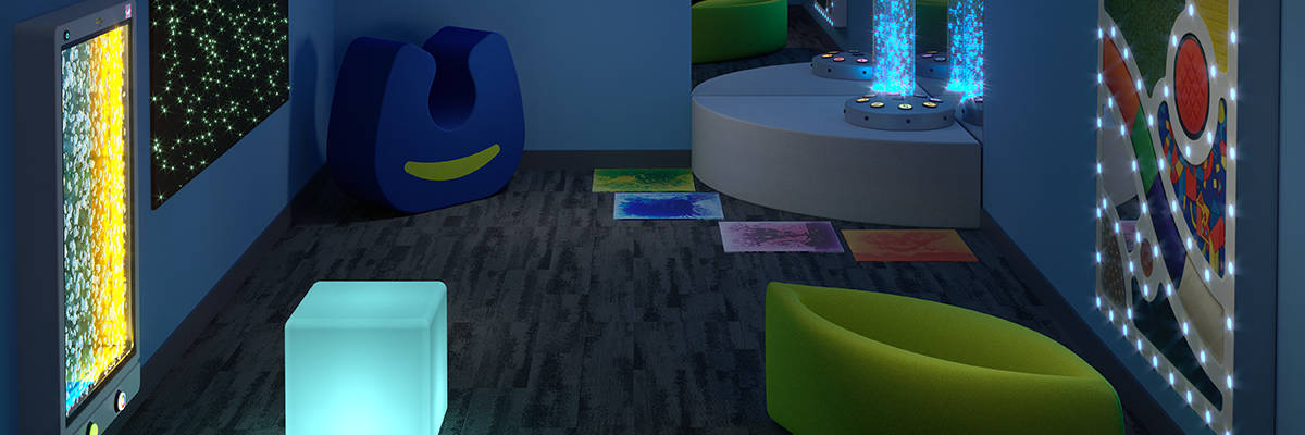 small sensory room with soft compression seating, sensory lights on the walls, a sensory cube and tiles on the floor, and bubble tubes