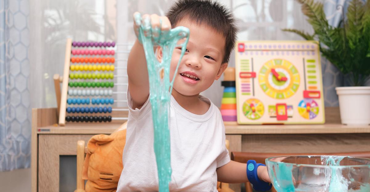 young boy smiling while playing with slime, behind him are other early childhood science and math toys