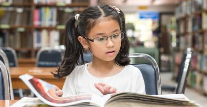 young student reading a book in a classroom library