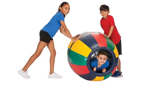 two children pushing a third child in a colorful play barrel