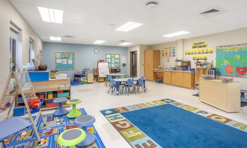 early childhood classroom with colorful rugs and decorations, wobble stools, and tables and chairs, alternate angle