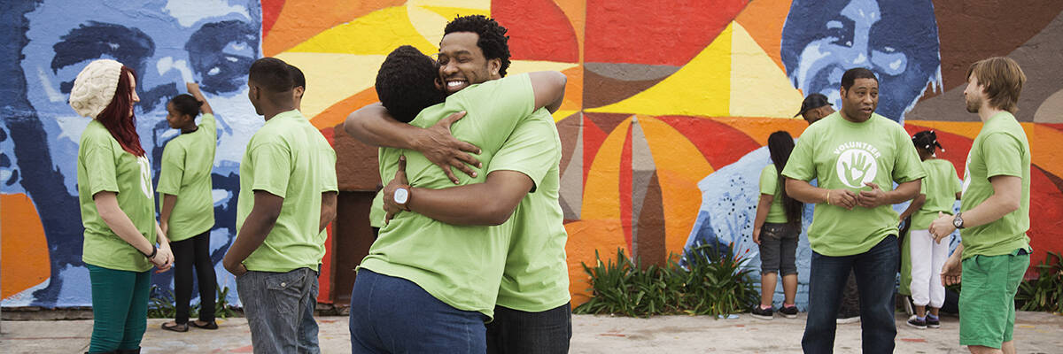 community members talking and hugging in matching green volunteer t-shirts in front of an outdoor mural