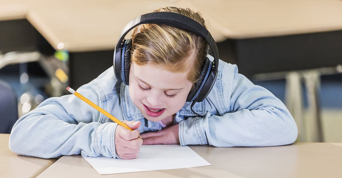 student writing with a pencil and wearing noise reduction headphones